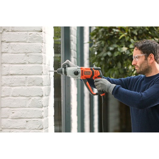Photo of BLACKDECKER BEHS02K hammer drill in use, drilling into a white brick wall outdoors.