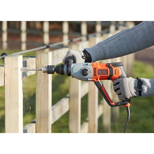 Photo of BLACKDECKER BEHS02K corded hammer drill in use drilling into a wooden fence outdoors.