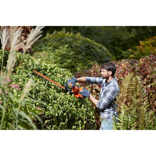 Photo of a person using BLACK+DECKER BEHT251KIT hedge trimmer on green bush in garden.