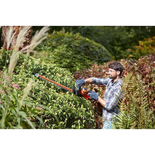 BLACKDECKER BEHTS451 hedge trimmer in use for trimming green garden bushes outdoors.