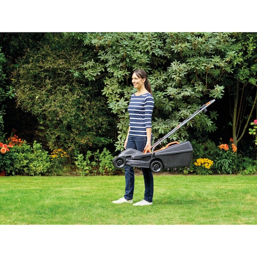 Photo of person carrying BLACKDECKER BEMW351GL2 lawn mower by handle in garden.