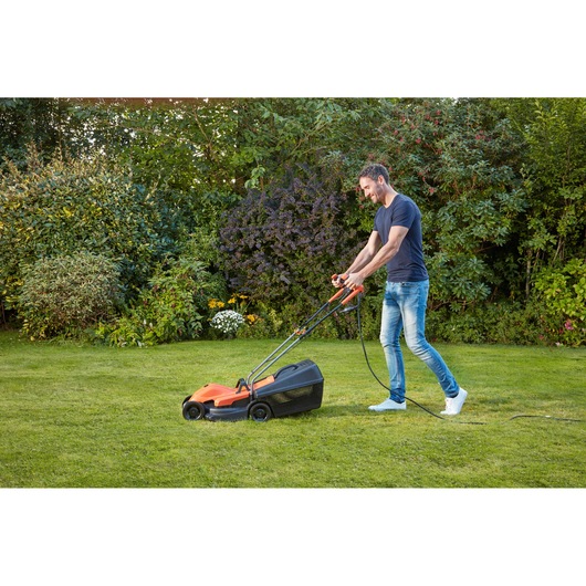 BLACKDECKER BEMW451BH lawn mower in use on grass garden, orange and black design, photography side view.
