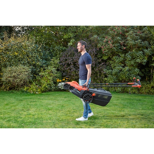 Photo of a person carrying a BLACKDECKER lawn mower BEMW461BGL2 in a garden setting.