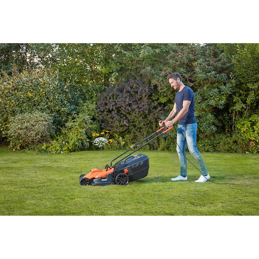 BLACKDECKER BEMW481BGL2 lawn mower in use on grass in a garden setting.