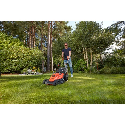 BLACKDECKER BEMW481BGL2 lawn mower in use on grass, orange and black design, outdoor garden setting.