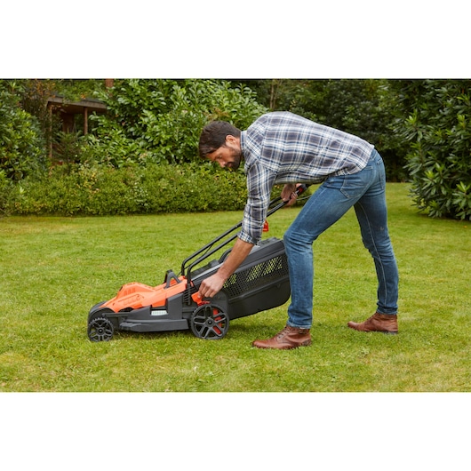 Photo of BLACKDECKER BEMW481BH lawn mower on grass with user adjusting height setting.