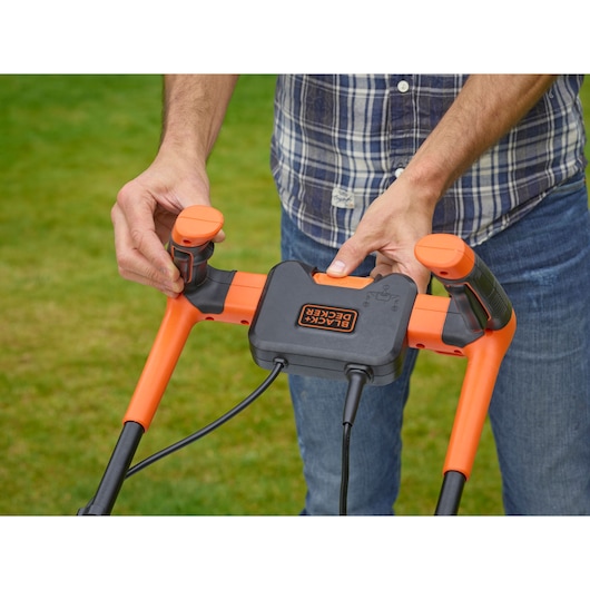 Close-up photo of BLACK+DECKER BEMW481BH lawn mower handle with orange and black controls in outdoor setting.