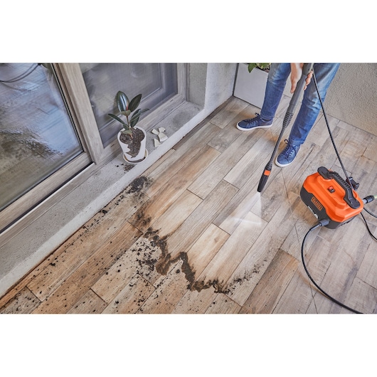 BLACKDECKER BEPW1300H pressure washer cleaning dirt from patio tiles, side angle, person holding wand.