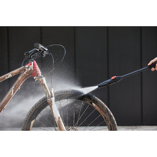 BLACKDECKER BEPW1300L pressure washer cleaning muddy bicycle wheel outdoors.