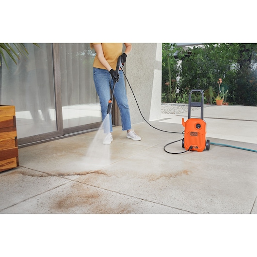 Photo of BLACKDECKER BEPW1300L pressure washer cleaning outdoor patio floor, person in jeans and gloves holding spray wand.