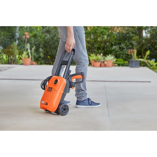 Photo of a person pulling a BLACKDECKER BEPW1300L orange portable pressure washer with wheels on a patio.