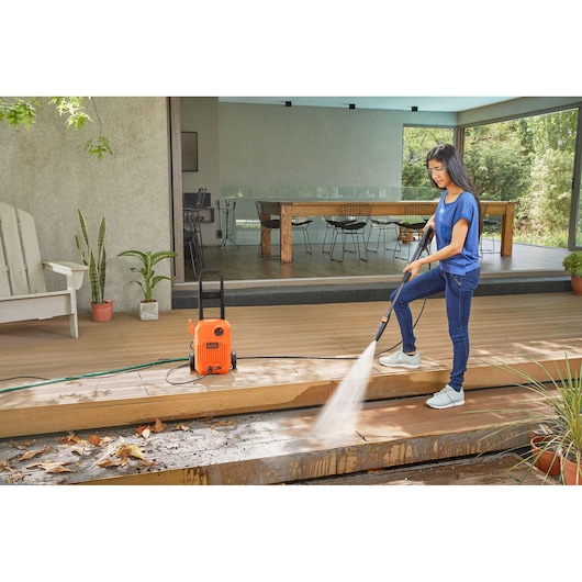 Photo of BLACKDECKER BEPW1650 pressure washer cleaning outdoor wooden deck, orange unit with hose and spray wand.