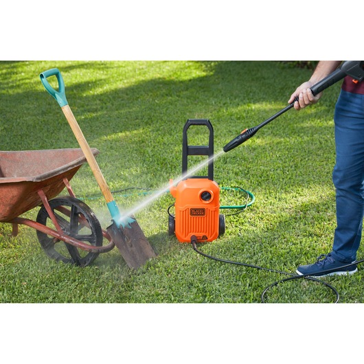 Photo of BLACKDECKER BEPW1650 pressure washer cleaning a shovel beside a wheelbarrow on a lawn.
