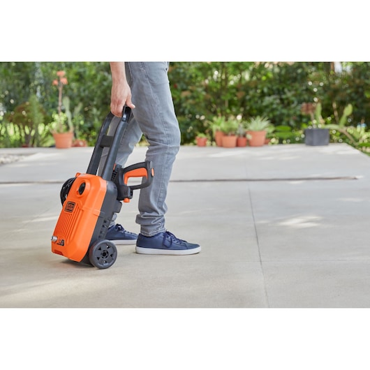Photo of a person wheeling a BLACK+DECKER BEPW1650 electric pressure washer with orange and black design on a patio.