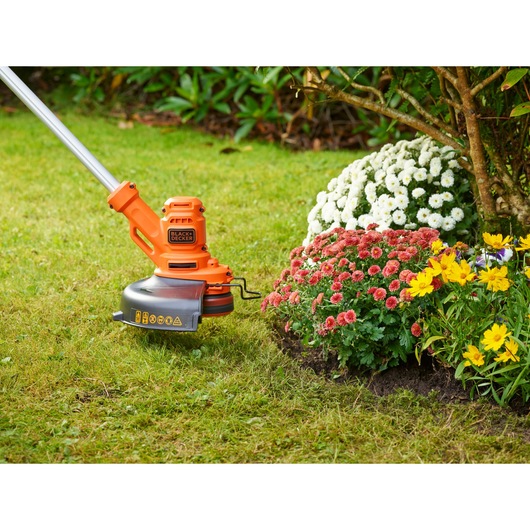 Photo of BLACK+DECKER BESTA525 grass trimmer in use edging a flower bed with colorful flowers in a garden.