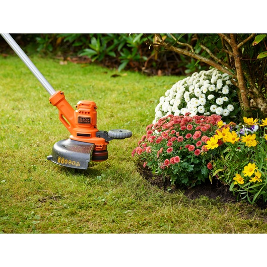 BLACKDECKER BESTA530C10 grass trimmer used for edging near colorful flower beds on a garden lawn.