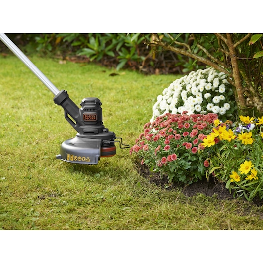 BLACKDECKER BESTE625 grass trimmer cutting lawn edge near colorful flower bed outdoors.