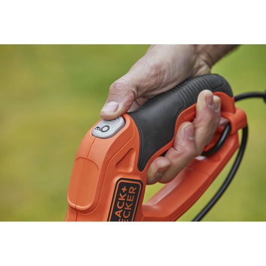 Close-up of BLACK+DECKER BESTE628 grass trimmer handle with hand pressing power button, orange and black design.