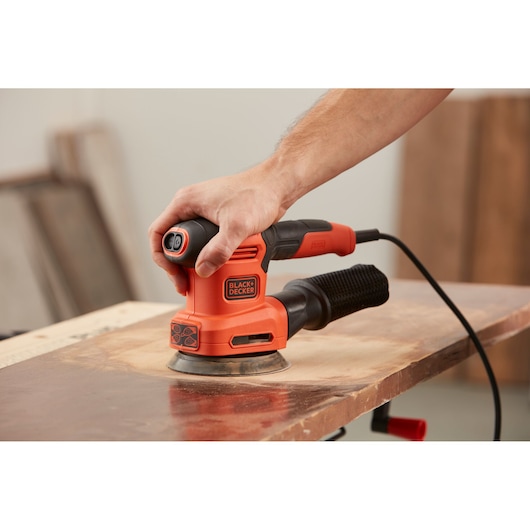 BLACKDECKER BEW200LSA orange electric sander in use on wood, close-up side angle.