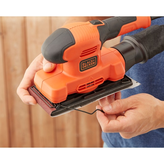 BLACK+DECKER BEW220 orange detail sander held in hand with sandpaper attachment.