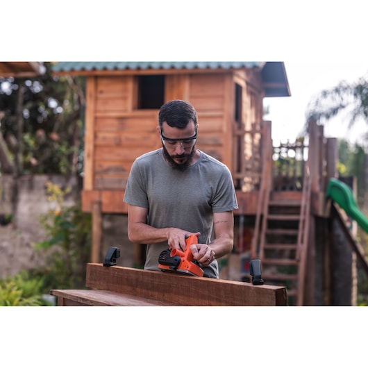 BLACKDECKER BEW712 power sander in use on wood plank outdoors, held by a person in gray shirt.