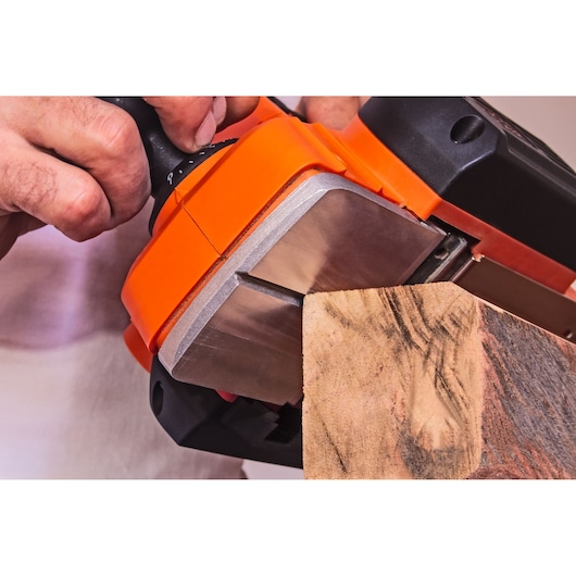 Photo of BLACK+DECKER BEW712 belt sander in use on a wooden plank, close-up angle.