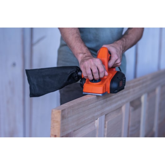 BLACKDECKER BEW712 electric planer in use on wooden door, side view, with dust bag attached.