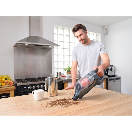BLACKDECKER BHFEA18D1 handheld vacuum cleaning coffee grounds on kitchen table in a modern kitchen.