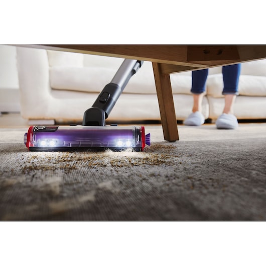 BLACKDECKER BHFEA640WG cordless vacuum cleaning debris under a table on carpet with LED lights on the floor head.