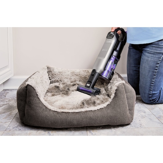 BLACKDECKER BHFEA640WP cordless vacuum used to clean fur from a gray plush pet bed on tile floor.