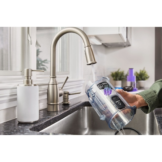 Photo of BLACKDECKER BHFEA640WP vacuum dustbin being rinsed under a kitchen faucet next to a soap dispenser.