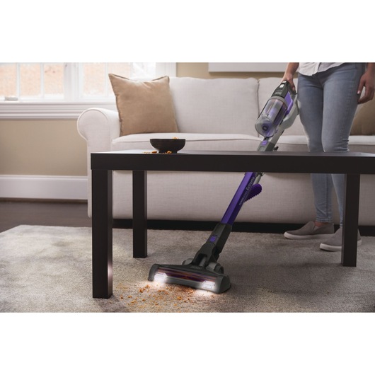 BLACKDECKER BHFEV362DP cordless stick vacuum cleaning crumbs from carpet under coffee table in living room.