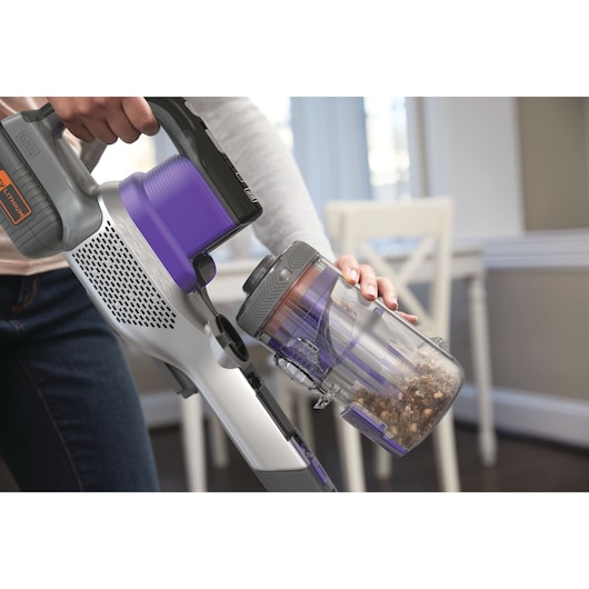 Photo of BLACKDECKER BHFEV362DP cordless vacuum with purple accents, showing dust canister being emptied indoors.