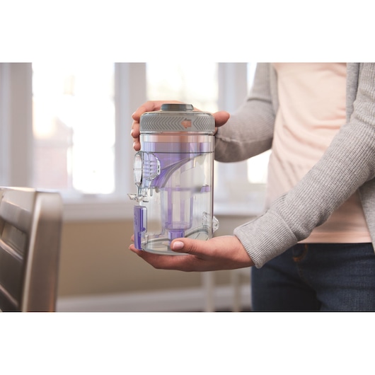Photo of person holding BLACKDECKER BHFEV362DP vacuum dust container with transparent body and purple accents.