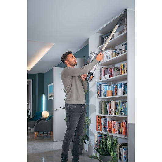 BLACKDECKER BHFEV36B2D cordless vacuum cleaning bookshelf corner in modern living room.