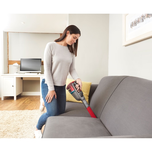 BLACKDECKER BHHV315J handheld vacuum cleaning grey sofa in living room.