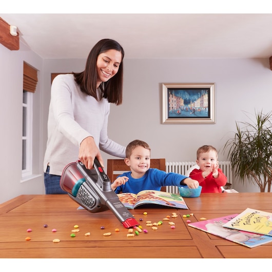 BLACKDECKER BHHV315J handheld vacuum cleaning colorful snack crumbs from a wooden dining table near children.