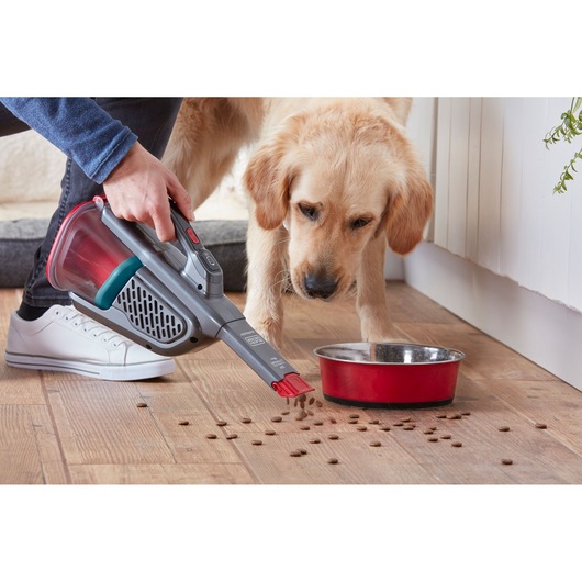 BLACKDECKER BHHV315J handheld vacuum cleaning pet food near red bowl on wood floor, side angle.