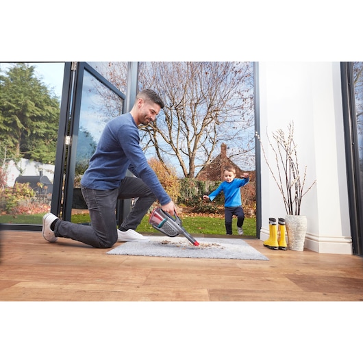 BLACKDECKER BHHV315J handheld vacuum being used to clean dirt on a rug near an open doorway.