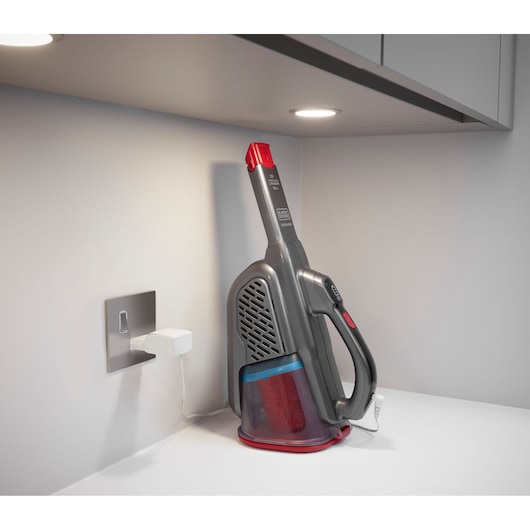 BLACKDECKER BHHV315J handheld vacuum in gray and red charging on a countertop, side view.