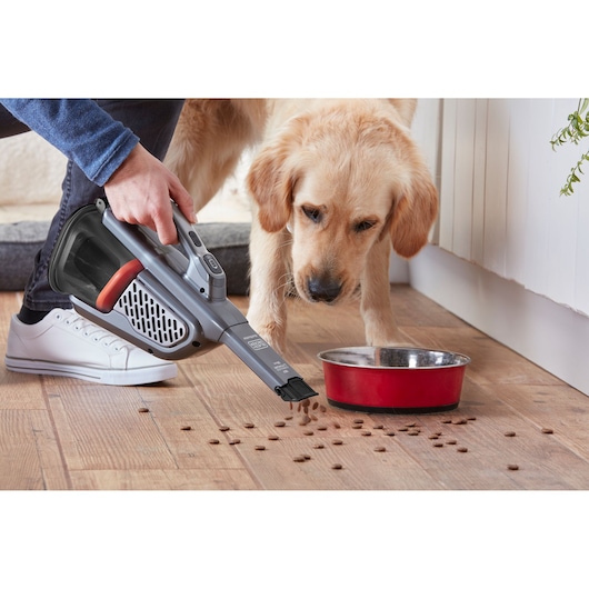BLACKDECKER BHHV520JF handheld vacuum cleaning pet food near red bowl on wooden floor, indoor scene.