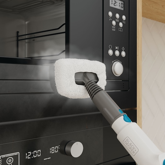 BLACK+DECKER BHSMP2314 steam cleaner with white cleaning pad cleaning black kitchen oven door.