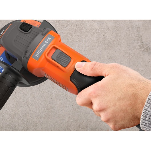 Close-up of a hand holding and operating an orange and black brushless power tool against a plain background.
