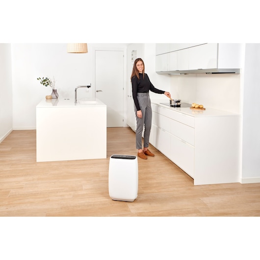 BLACKDECKER BXAP350E air purifier in white on wood floor in modern kitchen with person cooking in background.