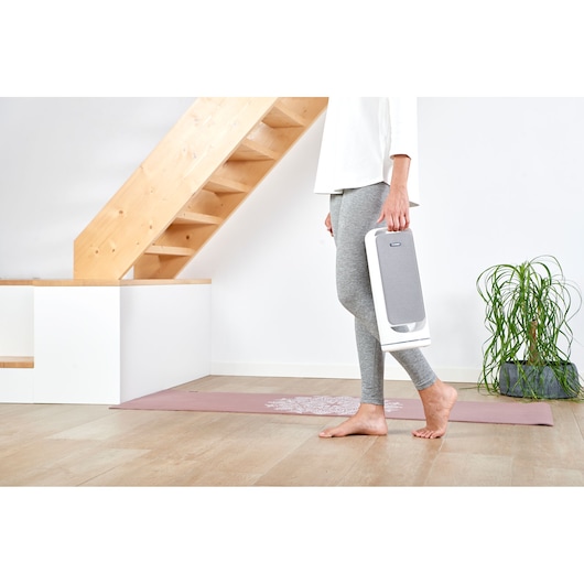 Photo of person holding BLACK+DECKER BXAP60E portable air purifier in a modern home interior.