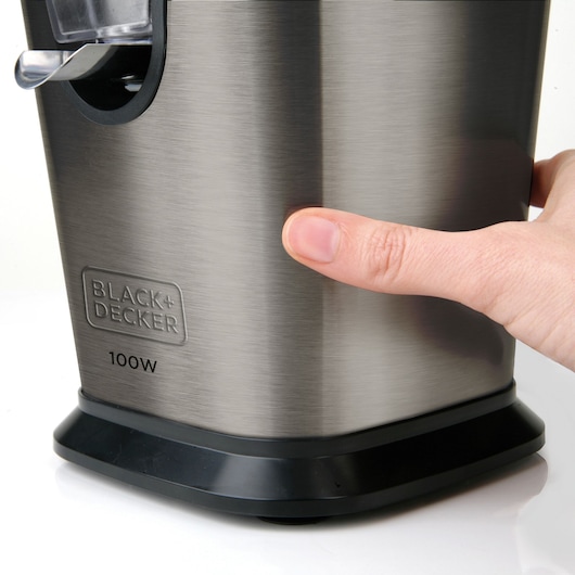 Photo of BLACK+DECKER BXCJ100E stainless steel citrus juicer close-up, hand pressing power button on base.