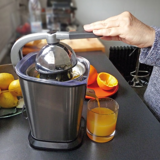 BLACKDECKER BXCJ100E citrus juicer with stainless steel body on kitchen counter, juicing oranges into glass, side angle.