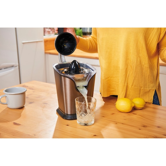 BLACKDECKER BXCJ100E citrus juicer pouring juice into glass on kitchen table, lemons beside.