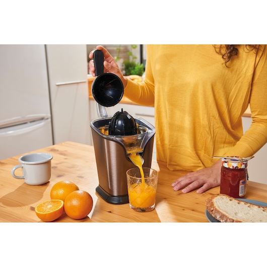 BLACKDECKER BXCJ100E citrus juicer making orange juice on kitchen table, oranges and bread visible.