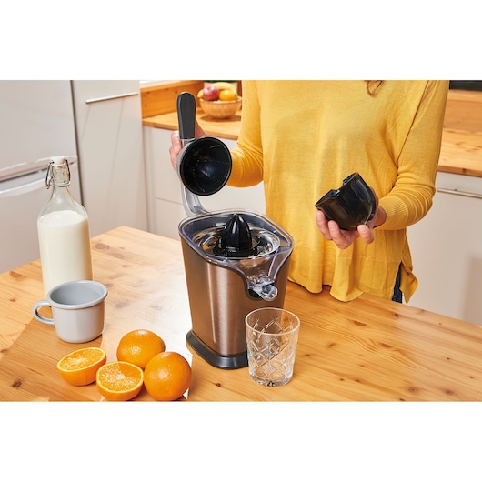 BLACKDECKER BXCJ100E citrus juicer on kitchen table with oranges, glass, and person assembling parts.